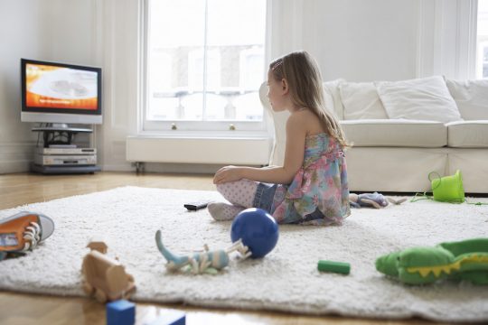 Young girl watching television alone and surrounded by toys